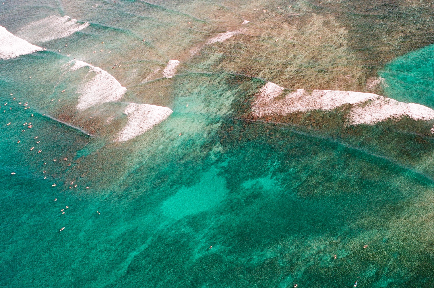 White waves break over a reef in clear turquoise water.